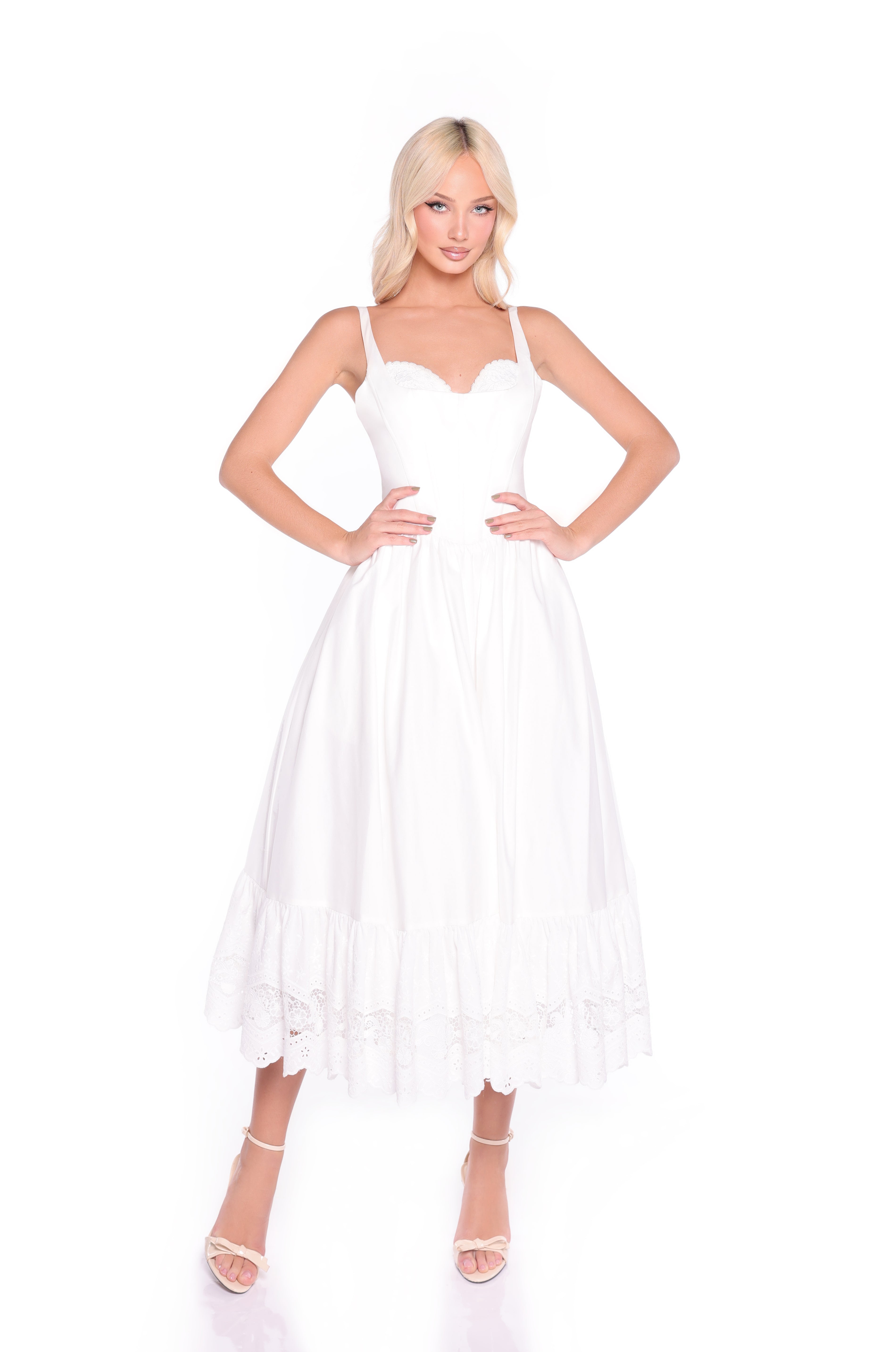 A woman poses against a white background wearing the White Casual Midi Dress: Celeste, featuring a corset bodice and ruffled hem, styled with white heeled sandals.
